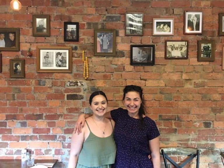 two sisters Eleftheria and Natalie Amanatidis in front of the wall of family photos at Eleni's Kitchen and Bar