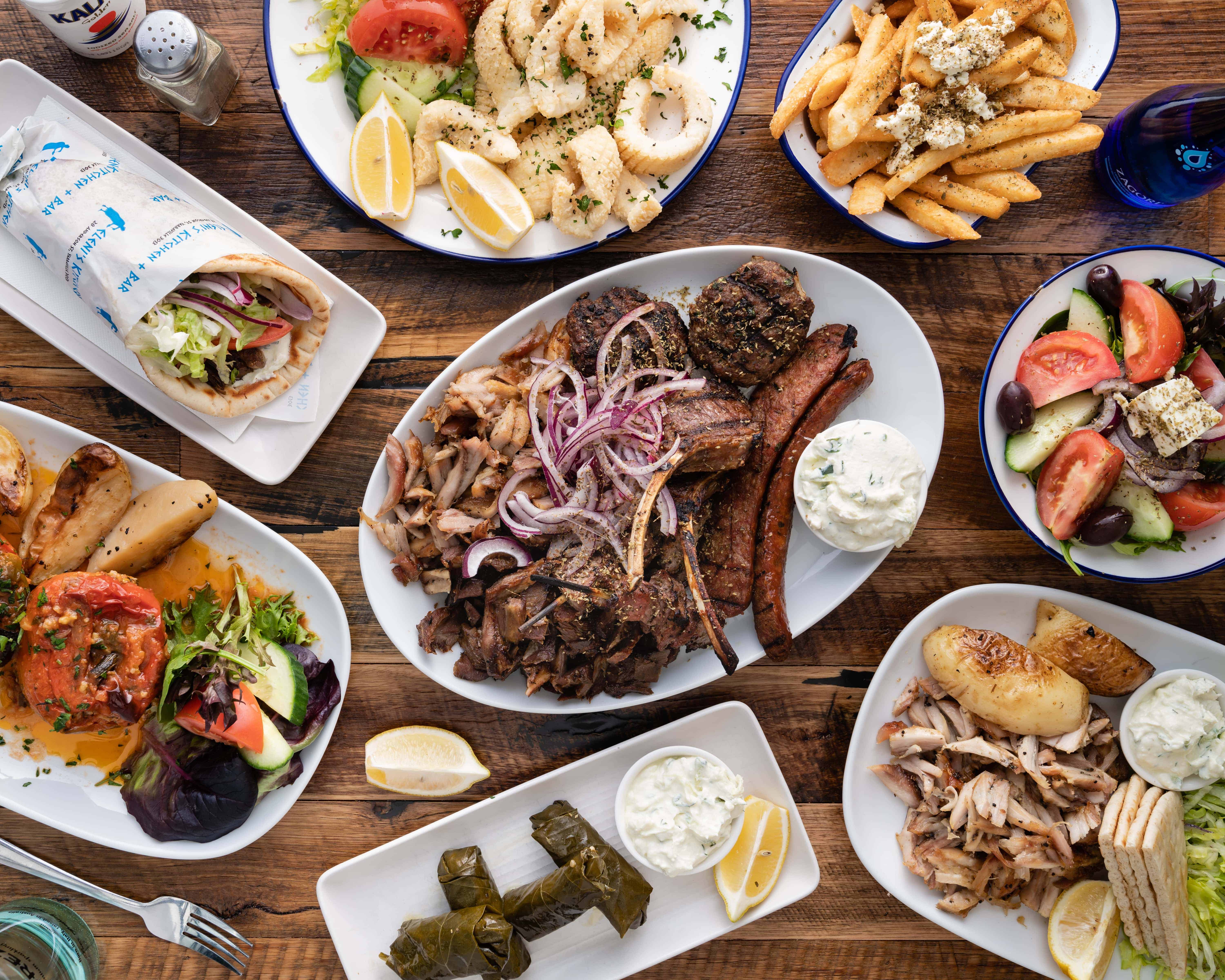 Table with authentic Greek dishes including gemista, gyros, souvlaki, feta fries, greek salad, dolmades and fired calamari