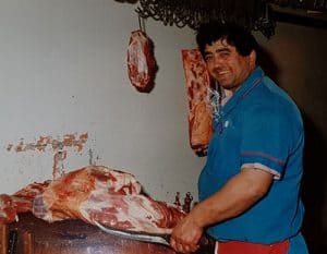 old photo of the butcher smiling and carving meat